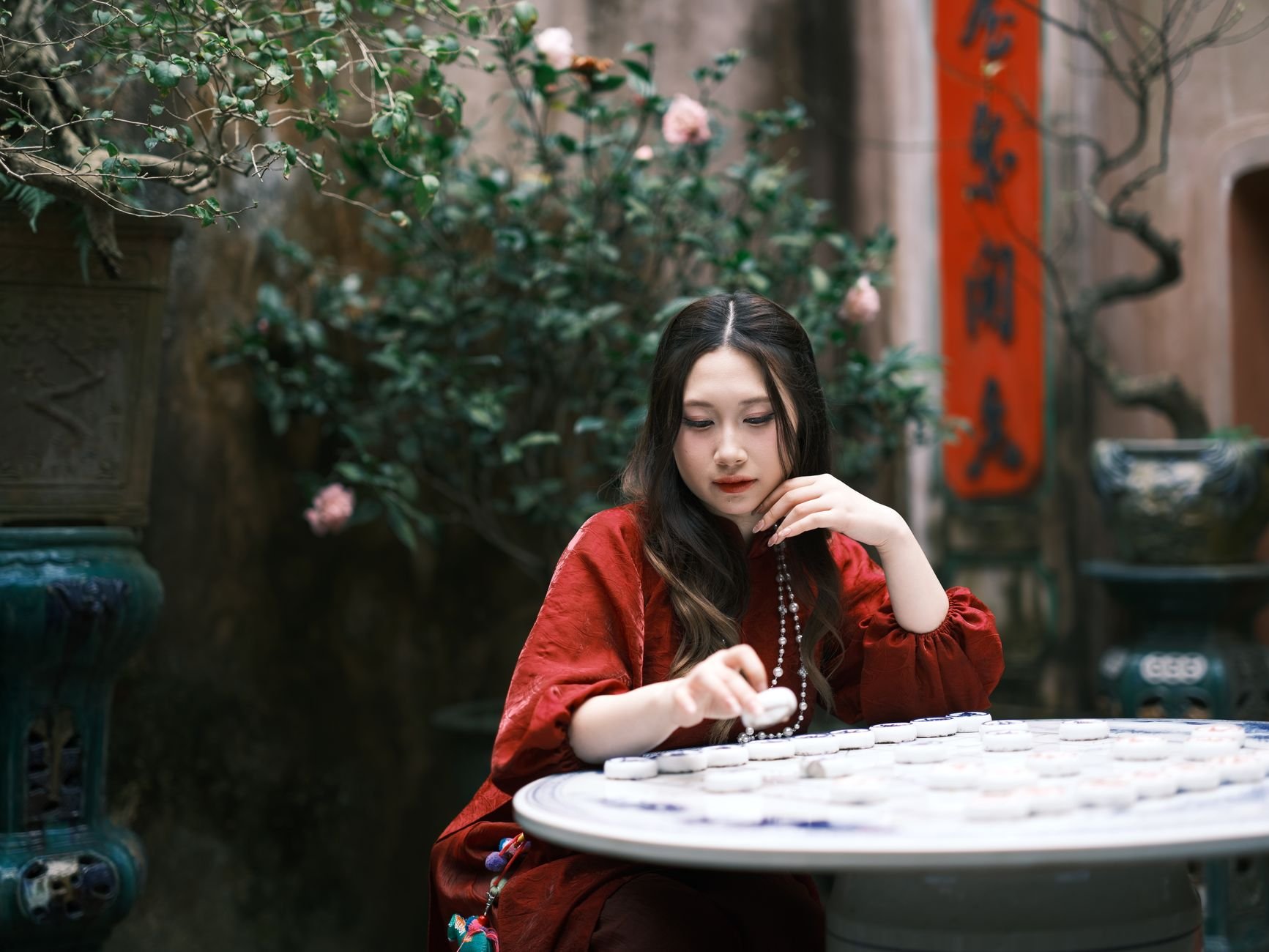 Woman in a red dress playing mahjong at a table surrounded by lush plants